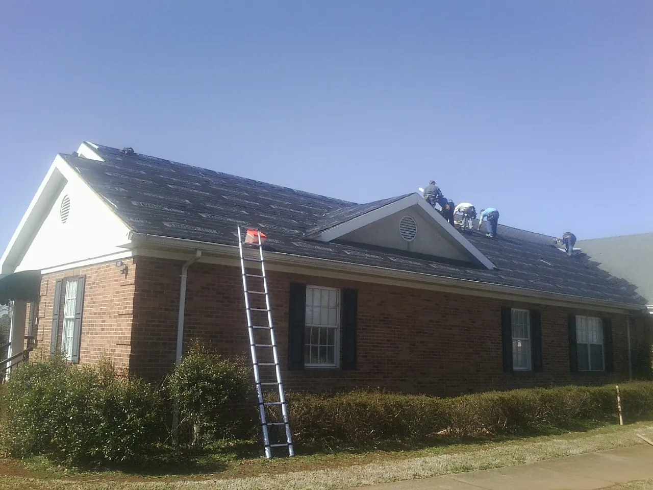Crew tearing shingles off a brick ranch roof with a ladder set — Metal Roof Repair work by our crew in New Tripoli