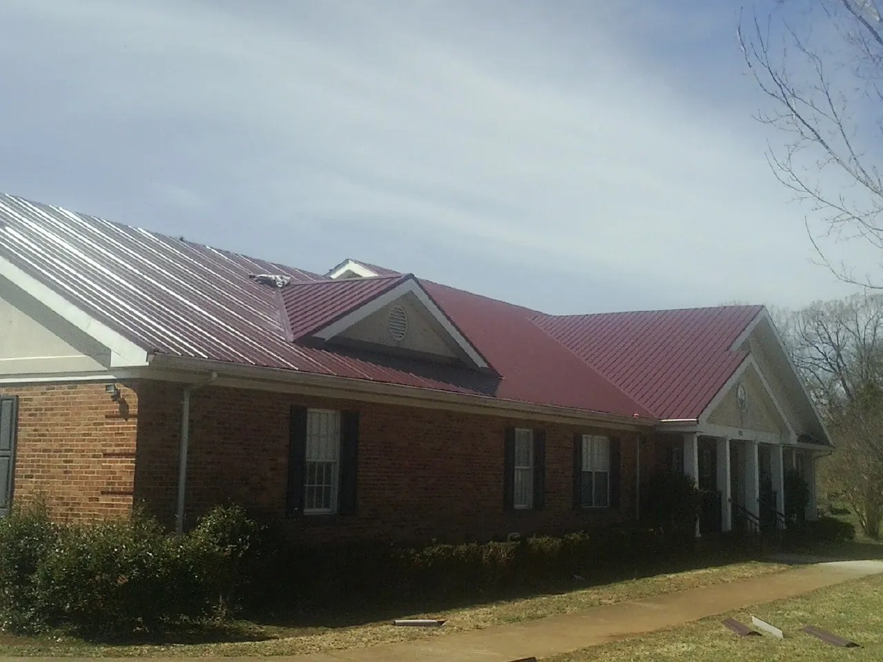 Red metal roof with gabled entries on a long brick building, from a Hail Damage Roof Repair job in New Tripoli