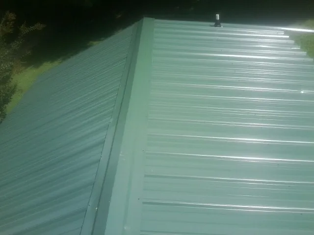 New green metal panels meeting at the ridge of a roof — Flat Roof Repair work by our crew in New Tripoli