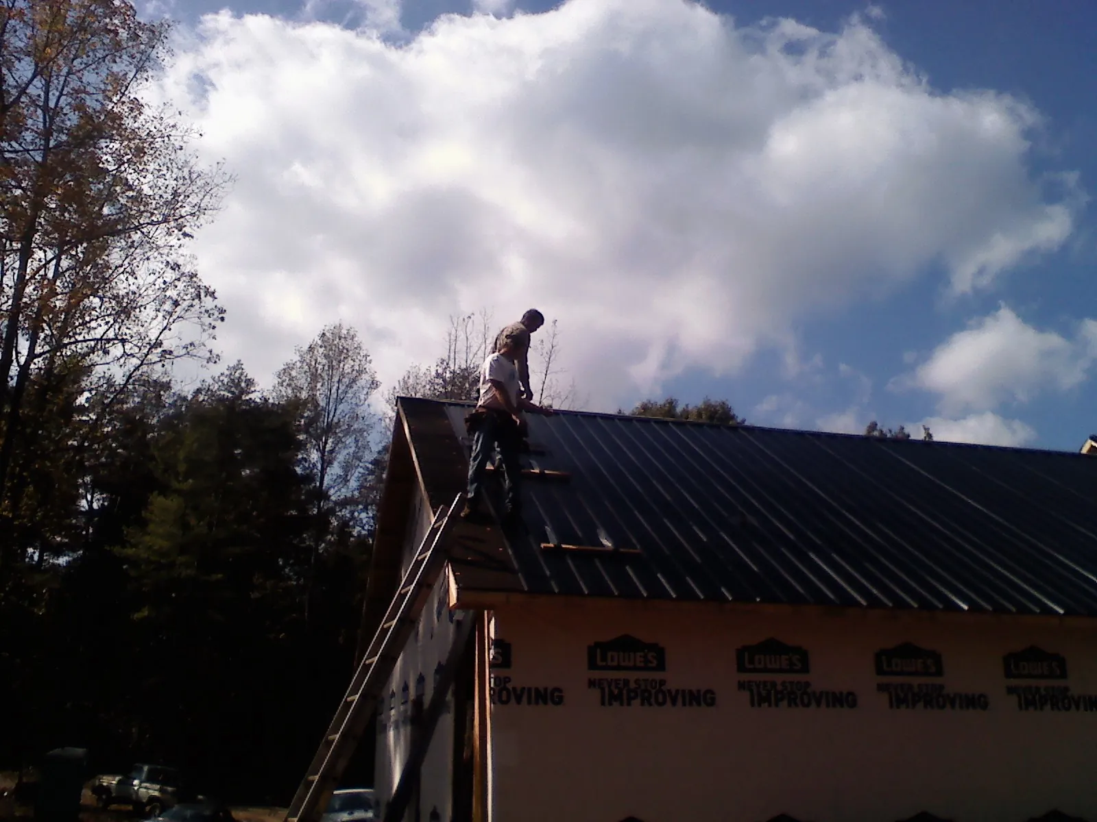 Roofer fastening dark metal panels high against a cloudy sky, from a Roof Inspection job in New Tripoli