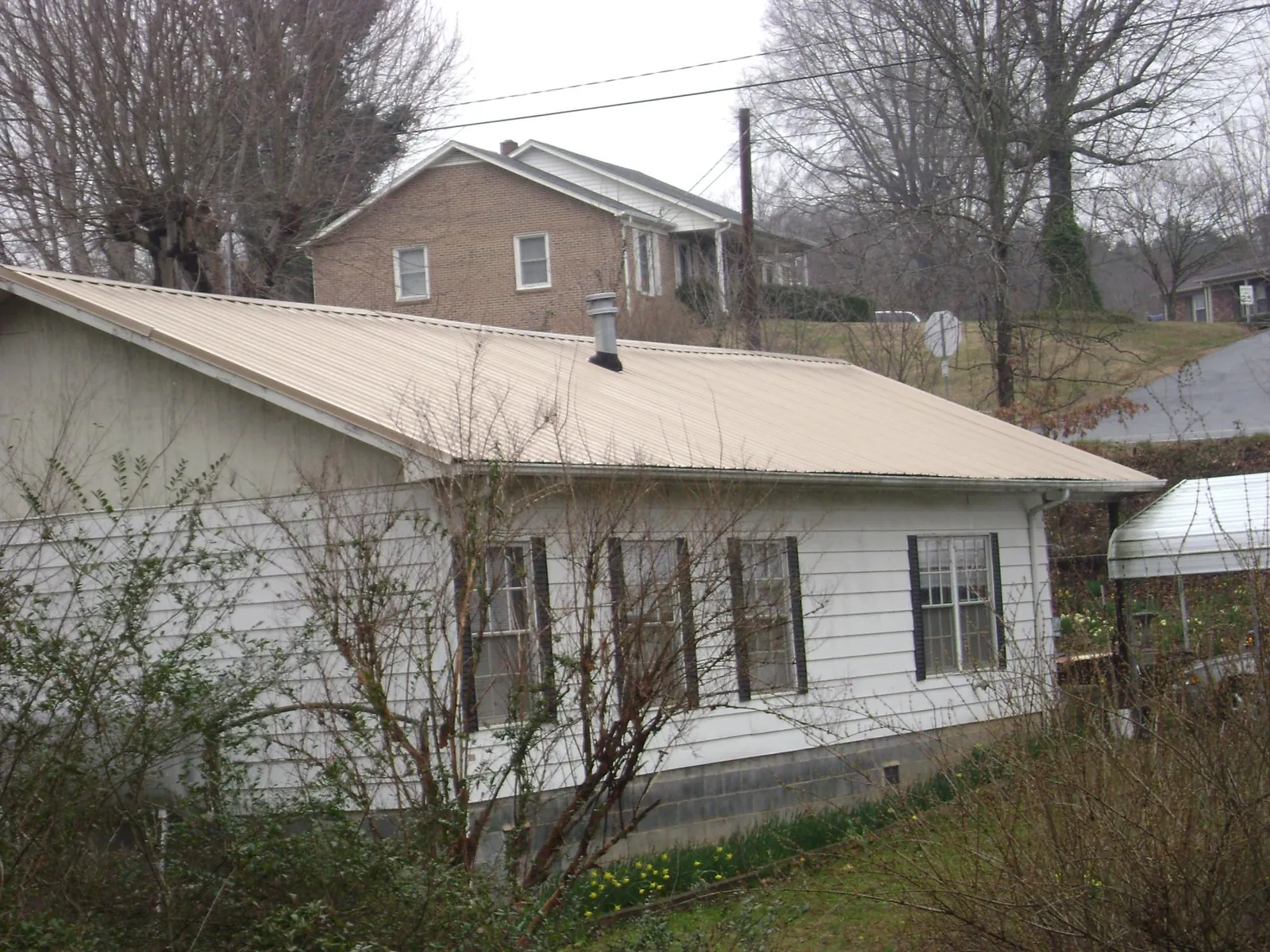 Tan metal roof on a white sided house set into a hillside — Commercial Roofing by Roofing Brothers in New Tripoli